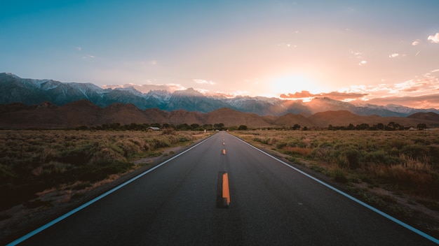 Carretera recta en medio del desierto con magníficas montañas y la puesta de sol