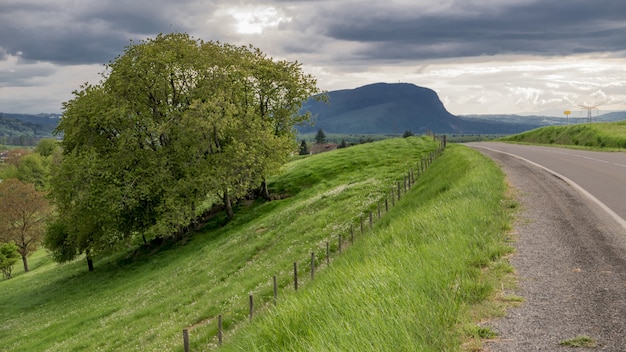 Foto gratuita carretera rodeada de campos verdes y montañas bajo el cielo sombrío