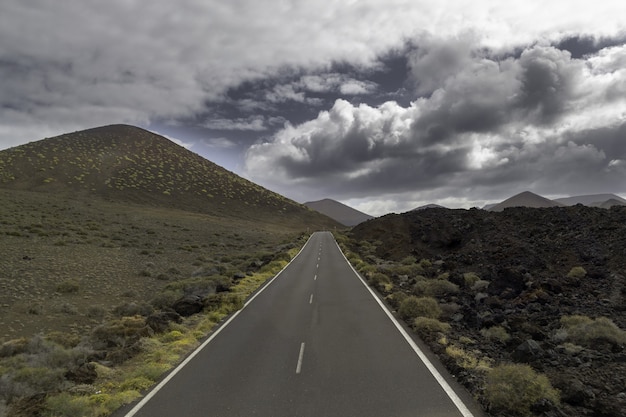 Carretera rodeada de colinas bajo un cielo nublado en el Parque Nacional de Timanfaya en España