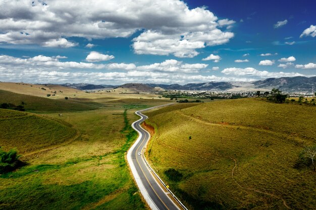 Carretera rodeada de colinas cubiertas de vegetación con montañas bajo un cielo nublado