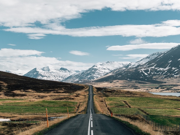 Carretera rodeada de colinas cubiertas de vegetación y nieve bajo un cielo nublado en Islandia