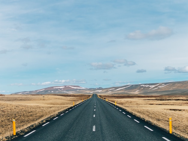 Carretera rodeada de colinas cubiertas de vegetación y nieve bajo un cielo nublado en Islandia