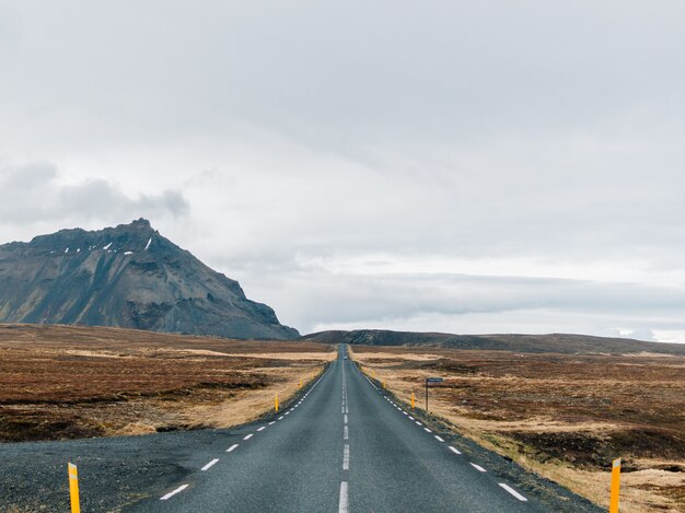 Carretera rodeada de colinas cubiertas de vegetación y nieve bajo un cielo nublado en Islandia