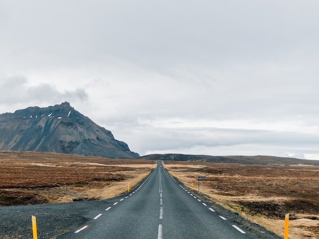 Carretera rodeada de colinas cubiertas de vegetación y nieve bajo un cielo nublado en Islandia