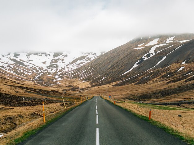 Carretera rodeada de colinas cubiertas de vegetación, nieve y niebla en Islandia