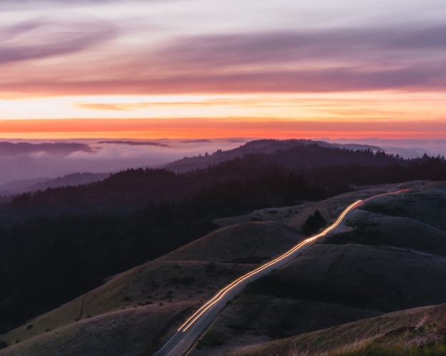 Carretera rodeada de colinas y luces con larga exposición durante una hermosa puesta de sol