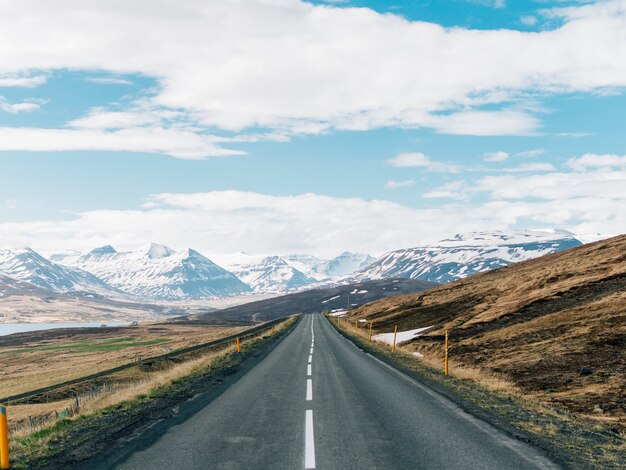 Carretera rodeada de colinas con montañas rocosas cubiertas de nieve.