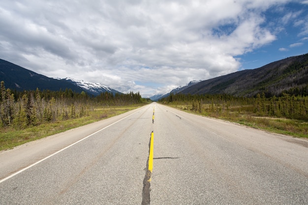 Carretera rodeada por un paisaje montañoso bajo el cielo nublado en Canadá