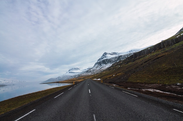 Carretera rodeada por el río y colinas cubiertas de nieve y hierba bajo un cielo nublado en Islandia