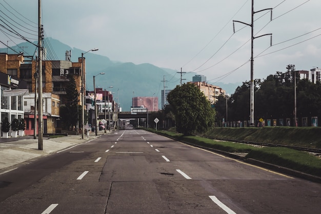 Carretera rodeada de vegetación y edificios con montañas bajo la luz del sol