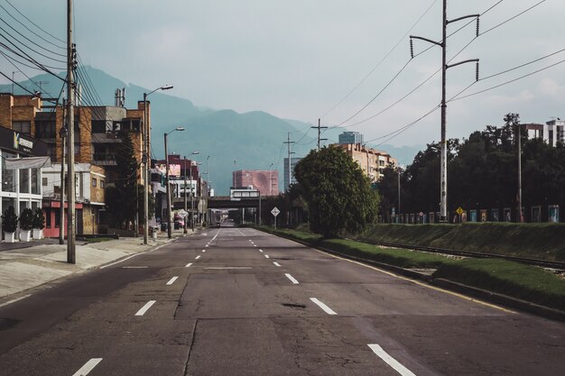 Carretera rodeada de vegetación y edificios con montañas bajo la luz del sol