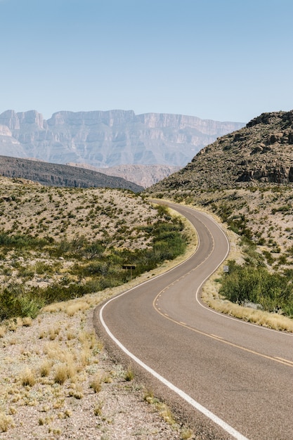 carretera vacía en medio de un campo seco con arbustos y montañas en la distancia