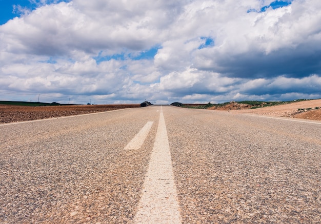 Carretera vacía rodeada de colinas bajo un hermoso cielo nublado