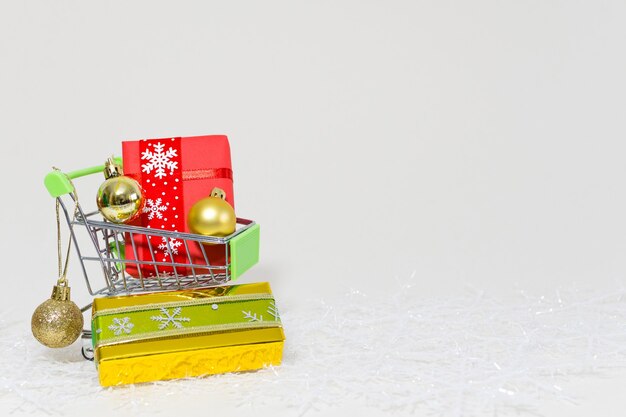 Carrito de la compra con cajas de regalo y esferas doradas sobre un copo de nieve sobre un fondo blanco.
