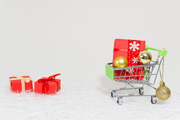 Carrito de la compra con cajas de regalo y esferas doradas sobre un copo de nieve sobre un fondo blanco.