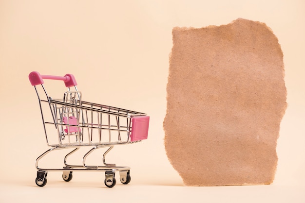 Un carrito de compras en miniatura vacío cerca de la pieza de papel rasgada contra un fondo de color