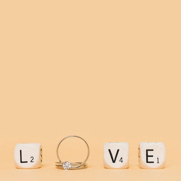 Carta de amor hecha con anillos de diamantes de boda y cubos sobre fondo crema.