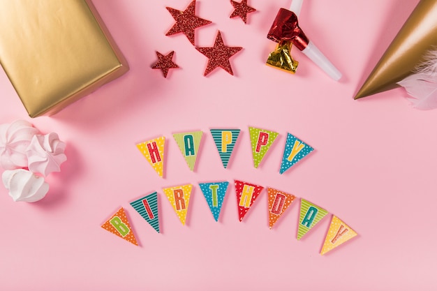 Carta de feliz cumpleaños con artículos de fiesta y zephyrs sobre fondo rosa