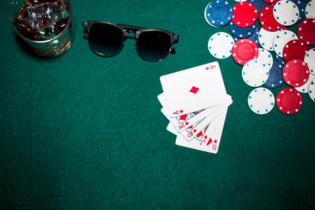 Carta de juego; fichas de casino; gafas de whisky y gafas de sol sobre fondo verde de póquer