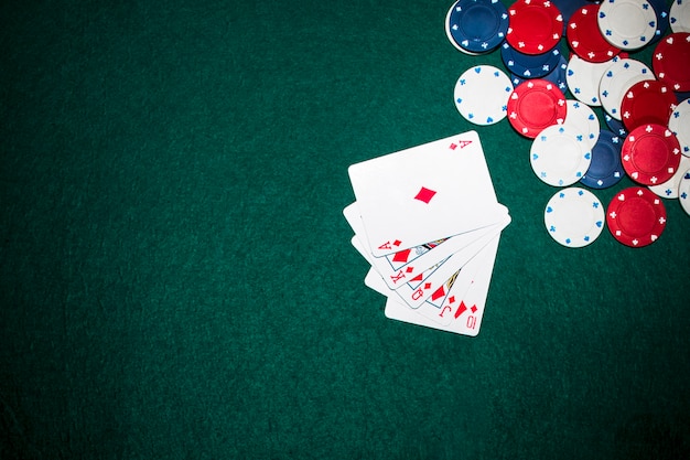 Cartas de juego de escalera real y fichas de casino en el fondo de póquer verde