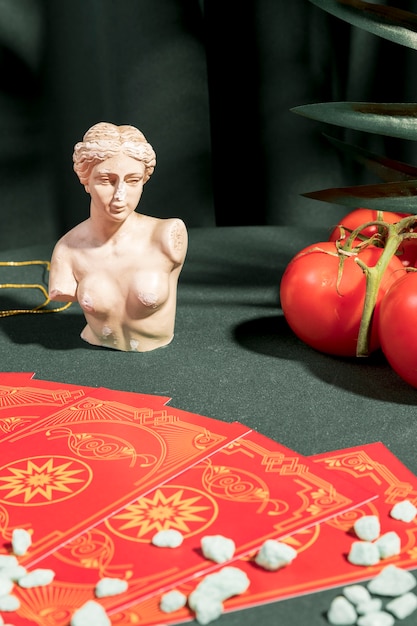 Cartas de tarot junto a busto y tomates.