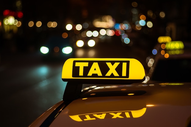 Cartel amarillo y negro de Taxi colocado encima de un coche por la noche