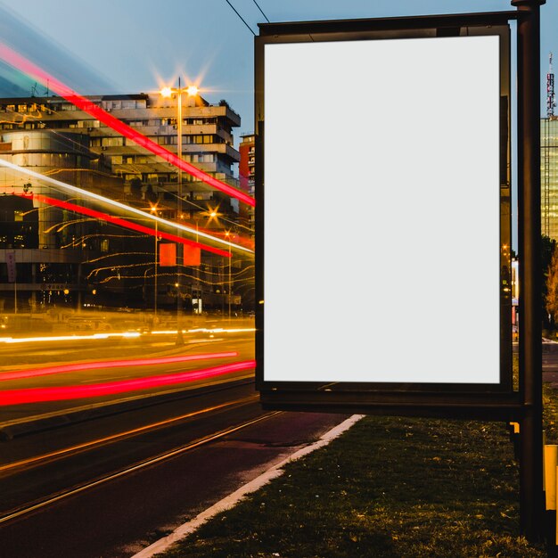 Un cartel blanco vacío con senderos de luz en la ciudad por la noche