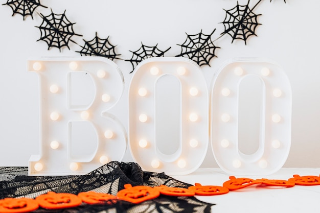 Foto gratuita cartel de boo iluminado sobre una mesa blanca con decoración de halloween