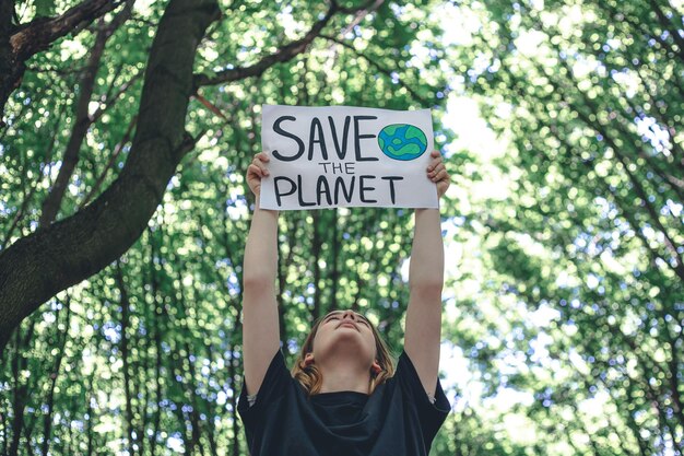 Cartel en la llamada para salvar el planeta en manos femeninas en el bosque