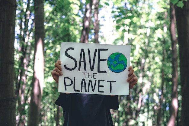 Cartel en la llamada para salvar el planeta en manos femeninas en el bosque