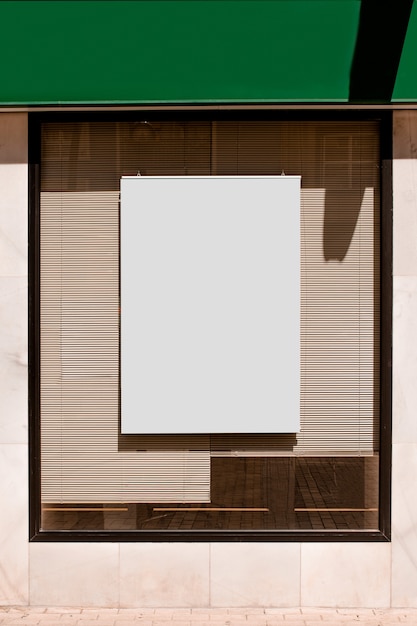 Cartelera rectangular en blanco en ventana de vidrio con persianas