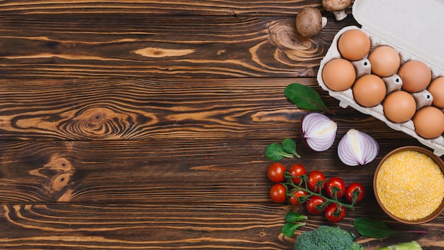 Carton de huevos; seta; polenta; Cebolla y brócoli en mesa de madera.