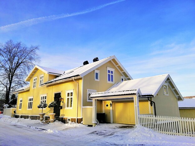 Casa amarilla rodeada de árboles cubiertos de nieve bajo un cielo nublado en Larvik en Noruega