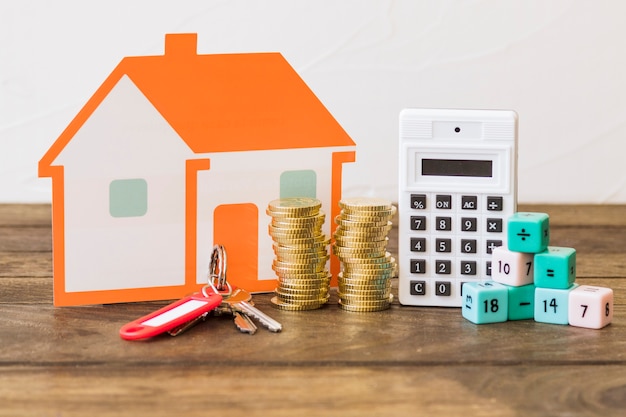 Foto gratuita casa, llave, monedas apiladas, calculadora y bloques de matemáticas en la mesa de madera