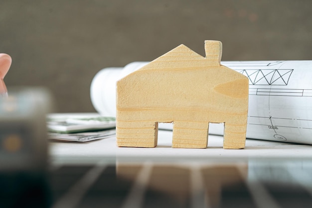 Casa de madera en miniatura y planos sobre mesa de madera