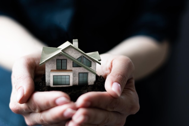 Casa modelo en mano de mujer, cajas en el fondo