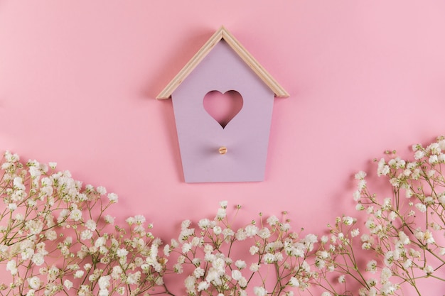 Casa del pájaro de la forma del corazón con las flores adornadas del gypsophila en fondo rosado