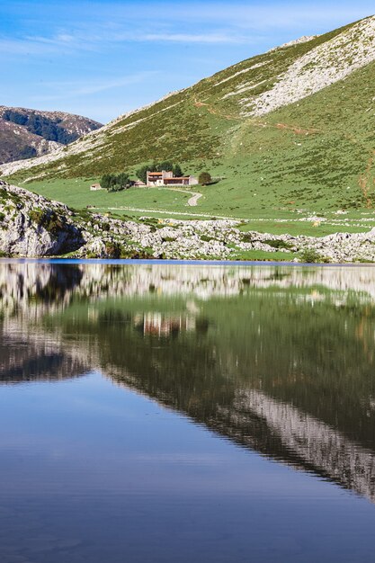 Una casa rodeada de un hermoso paisaje y su reflejo en el lago Enol en España