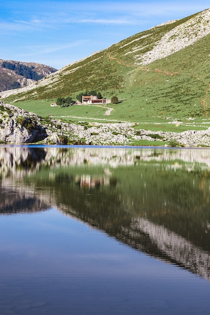 Una casa rodeada de un hermoso paisaje y su reflejo en el lago Enol en España