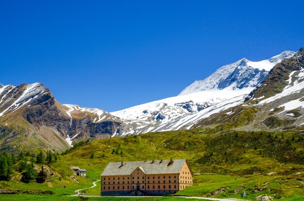 Casa rodeada de montañas rocosas cubiertas de vegetación y nieve en Valais en Suiza