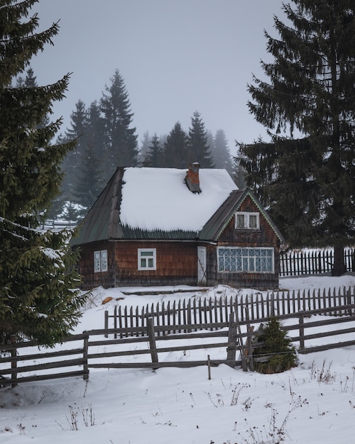 Casa con valla de madera en medio de pinos y nieve