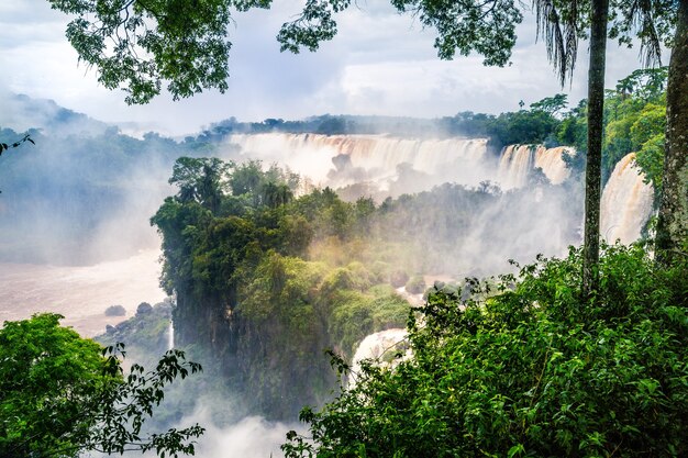 Cascada en el Parque Nacional Iguazú rodeado de bosques cubiertos de niebla bajo un cielo nublado