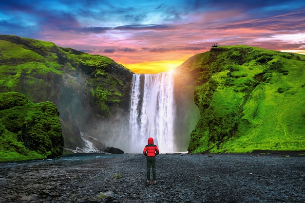 Cascada de Skogafoss en Islandia. Chico de chaqueta roja mira la cascada de Skogafoss.