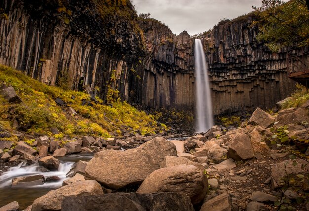 Cascada Svartifoss rodeada de rocas y vegetación bajo un cielo nublado en Skaftafell en Islandia