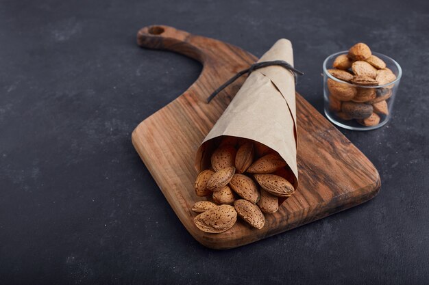 Cáscaras de almendras en la envoltura de papel y vaso de vidrio sobre tabla de madera sobre superficie azul.