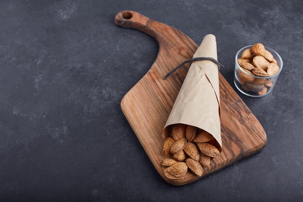 Cáscaras de almendras en la envoltura de papel y vaso de vidrio sobre tabla de madera.