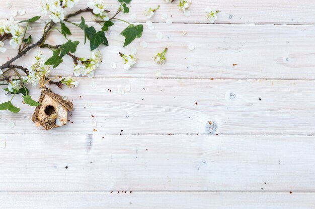 Casita para pájaros y ramas con flores en una mesa de madera con copyspace