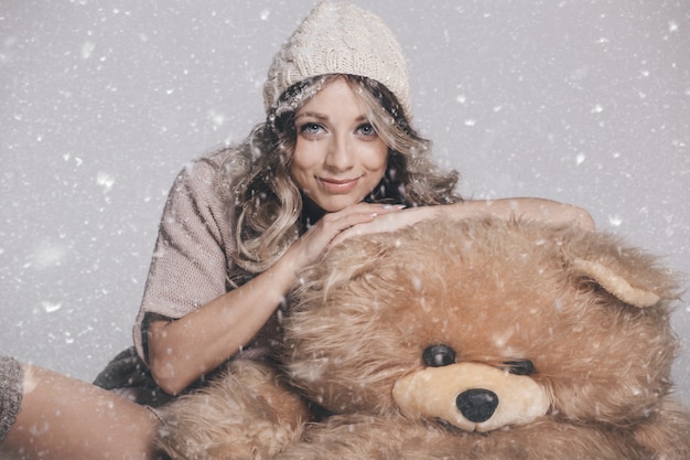 Casual joven sonriente en ropa de punto con gran oso de peluche suave sobre fondo nevado