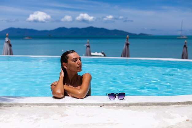 Caucásica mujer bronceada piel de bronce brillante junto a la piscina en bikini azul en un día soleado