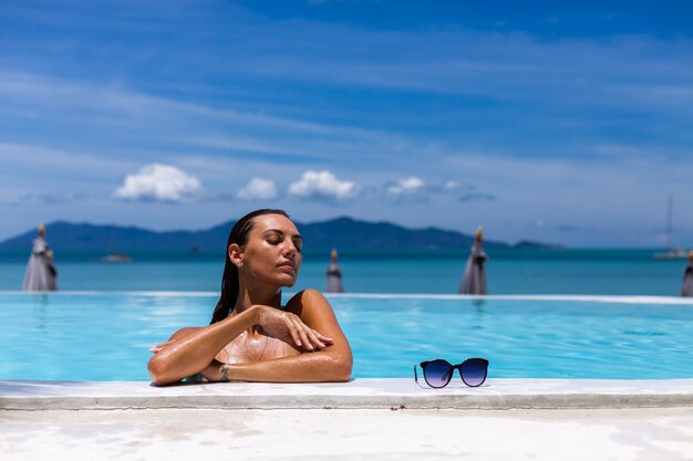 Caucásica mujer bronceada piel de bronce brillante junto a la piscina en bikini azul en un día soleado